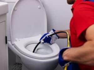 un uomo usa uno sturalavandini a molla nel wc per rimuovere un intasatura della fogna