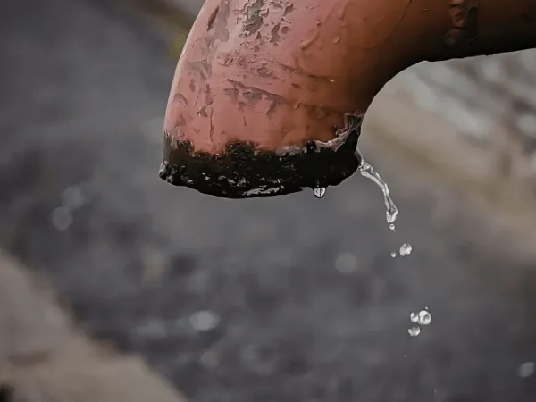 Primo piano di una perdita idrica da una tubazione esterna ammalorata con gocciolamento costante d'acqua.